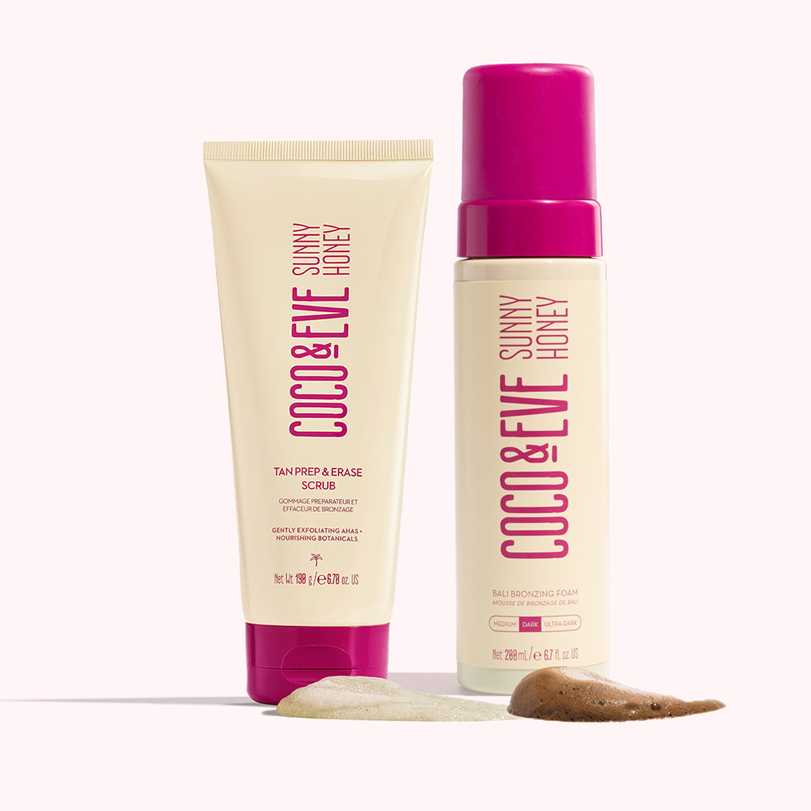 Two skincare bottles from Coco & Eve Sunny Honey line, one tan prep & erase scrub and one tan-exfoliating foam, displayed with a smear of tan scrub and exfoliating cream on a pale pink background.