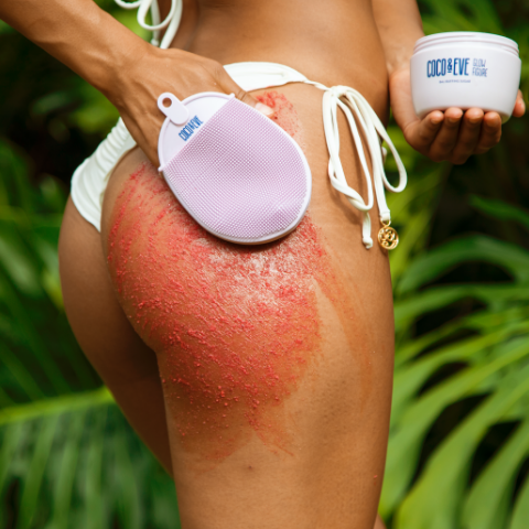 woman in bathing suit using silicone massage glove to exfoliate with bali buffing sugar